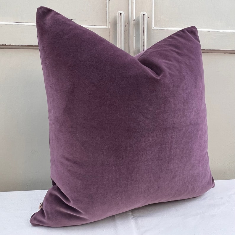 May include: A plush purple cushion with a soft, velvety texture. The cushion is square-shaped and has a subtle sheen.