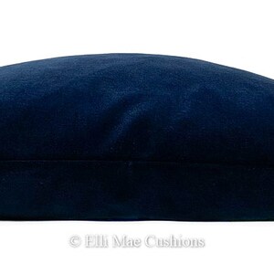 May include: A dark blue velvet cushion with a smooth, soft texture. The cushion is rectangular and has a subtle sheen.