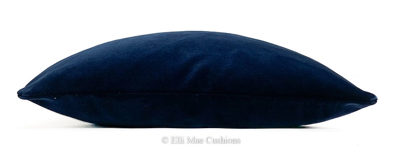 May include: A dark blue velvet cushion with a smooth, soft texture. The cushion is rectangular and has a subtle sheen.