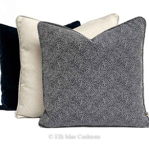 May include: Three decorative throw pillows. One pillow is navy blue with a white polka dot pattern. One pillow is beige with a white geometric pattern. One pillow is solid navy blue.