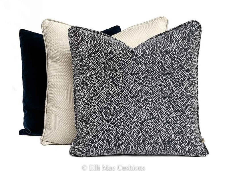 May include: Three decorative throw pillows. One pillow is navy blue with a white polka dot pattern. One pillow is beige with a white geometric pattern. One pillow is solid navy blue.