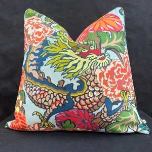 May include: Decorative throw pillow featuring a colorful dragon design. The pillow has a light blue background with a detailed illustration of a dragon in shades of yellow, red, brown, and blue. Floral elements in orange and green complete the design.