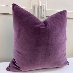 May include: A plush purple velvet cushion with a square shape. The cushion is soft and has a smooth texture.