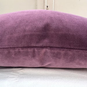 May include: A soft, plush purple cushion with a subtle sheen. The cushion is made of a velvet-like fabric and has a simple, rectangular shape.