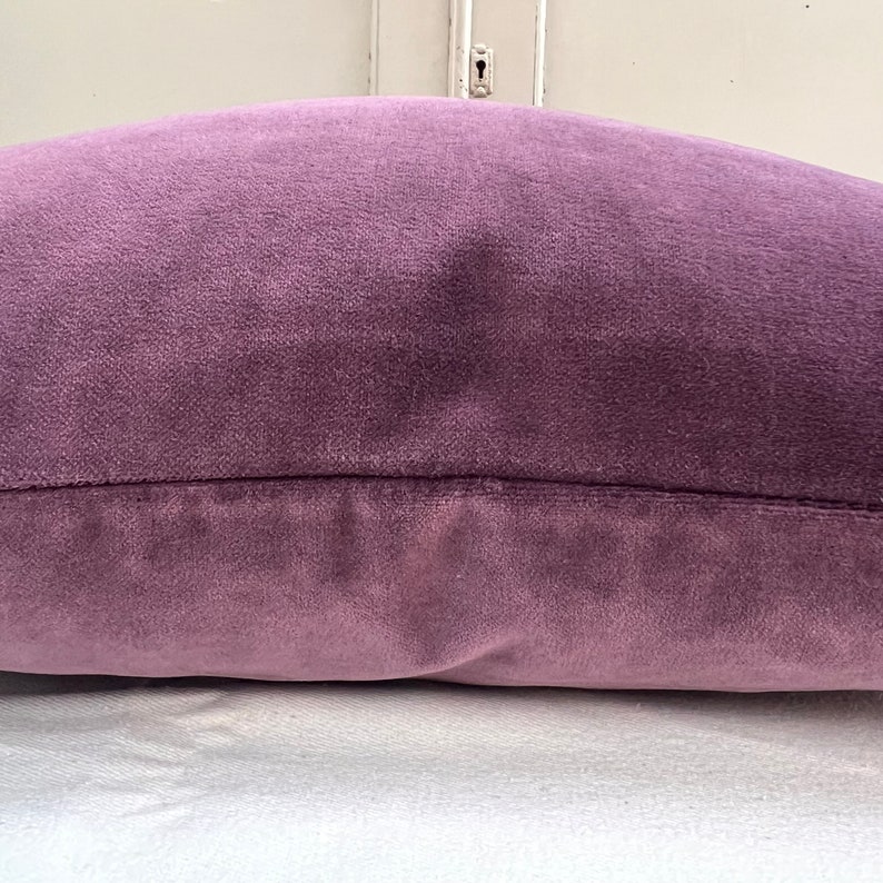 May include: A soft, plush purple cushion with a subtle sheen. The cushion is made of a velvet-like fabric and has a simple, rectangular shape.