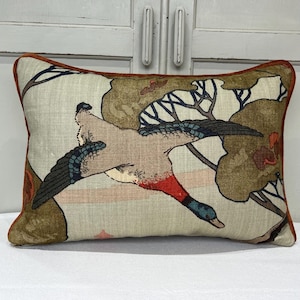 May include: A rectangular throw pillow with a brown, green, and blue design featuring a flying duck and leafy branches. The pillow has a rust-colored border.