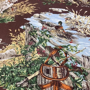 May include: Brown fabric with a detailed nature scene featuring ducks, a stream, and a fishing basket. The design includes a wooden fence, tall grass, and a fishing rod, creating a rustic, outdoorsy theme.