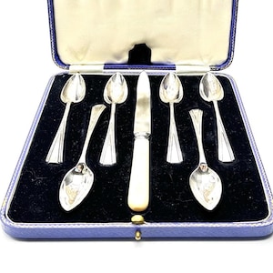 May include: A set of six silver teaspoons and a silver knife in a blue velvet lined box. The spoons have a rounded bowl and a fluted handle. The knife has a bone handle.