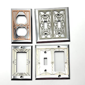 May include: Four decorative light switch plates with different Art Deco designs. The plates are made of metal and have a polished finish. The designs are in shades of silver, gold, and copper.