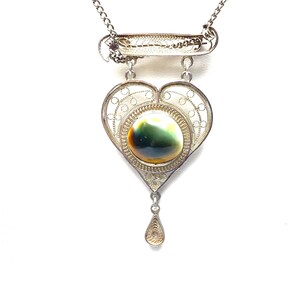 May include: A silver filigree heart pendant necklace with a green and brown stone in the center. The pendant has a teardrop-shaped charm hanging from the bottom.