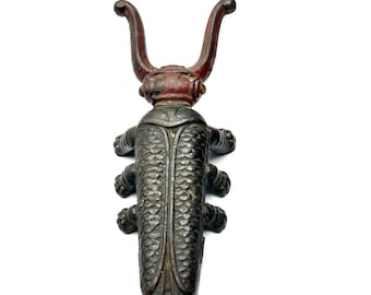 May include: A cast iron boot pull shaped like a beetle. The boot pull is painted in shades of black and red. The beetle has a textured body and six legs. The pull has two curved handles.