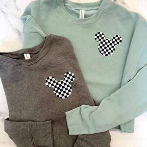 May include: Two cropped sweatshirts with a checkered Mickey Mouse design. One sweatshirt is gray and the other is light blue.