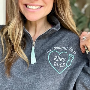 May include: A dark gray sweatshirt with a teal heart design that says "Ultrasound Tech Riley RDCS".