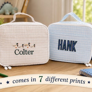May include: Two rectangular lunch bags with top handles and zipper closures. The left bag is beige gingham with an embroidered duck motif and the name Colter. The right bag is light blue gingham with the name HANK embroidered in dark blue letters.