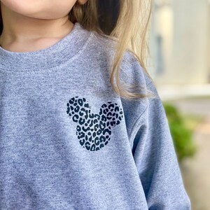 May include: A grey sweatshirt with a black and white leopard print Mickey Mouse design on the front.