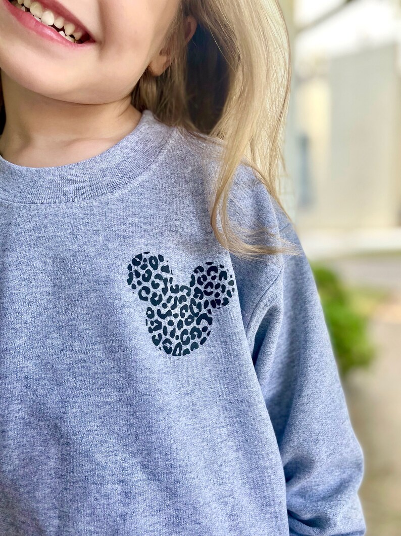 May include: A grey sweatshirt with a black and white leopard print Mickey Mouse design on the front.