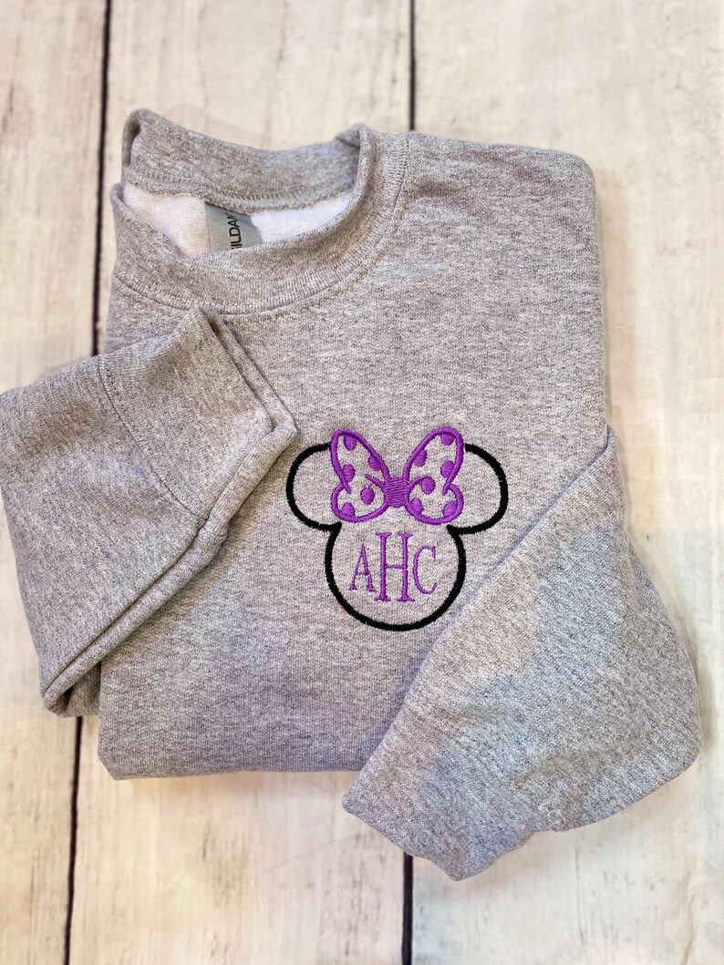 May include: Gray sweatshirt with a purple and white polka dot bow and black outline, with the letters AHC embroidered in black.