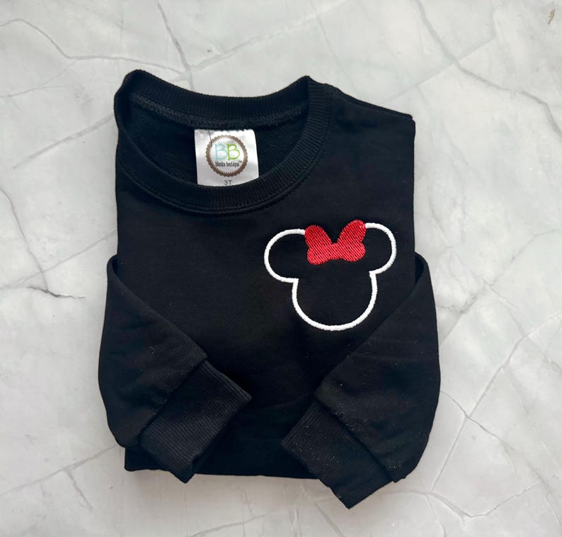 Op de afbeelding: Zwart sweatshirt met een witte omtrek van een muizenkop en een rode strik. De sweatshirt heeft lange mouwen en een ronde hals. Het label leest "BB Kids Design" en "3T".