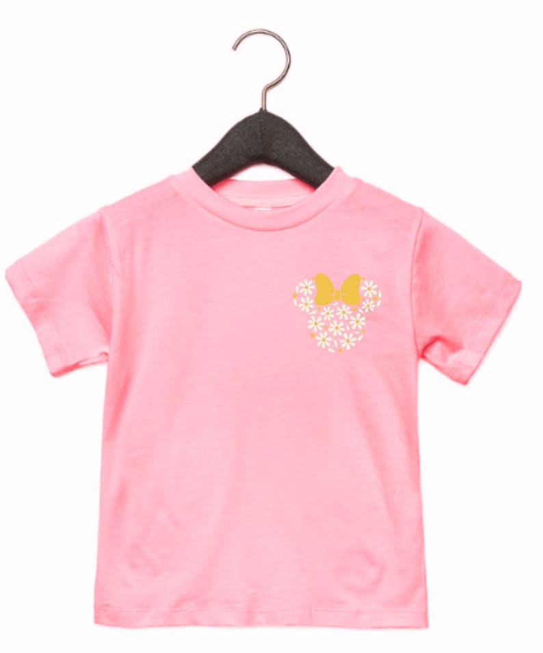 May include: Pink short-sleeved t-shirt with a floral Minnie Mouse design on the front. The design features white flowers and a yellow bow.