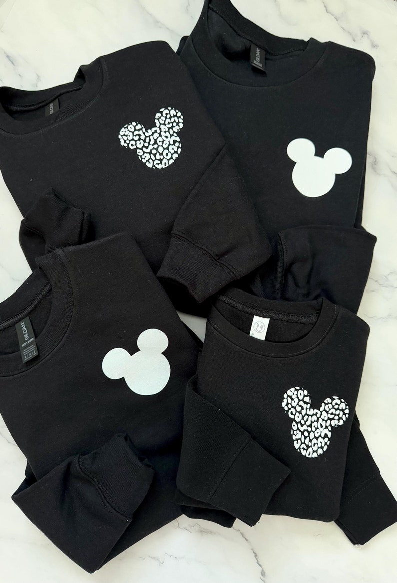 May include: Four black sweatshirts with different white Mickey Mouse designs. One sweatshirt has a solid white Mickey Mouse, one has a leopard print Mickey Mouse, and two have a white Mickey Mouse with a leopard print outline.