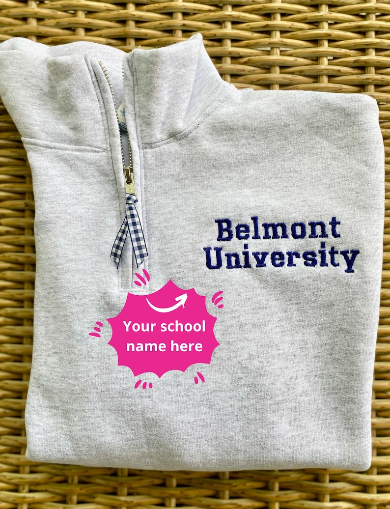 May include: Gray sweatshirt with a zipper and a blue embroidered logo that says "Belmont University". There is a pink speech bubble with an arrow pointing to the right that says "Your school name here".