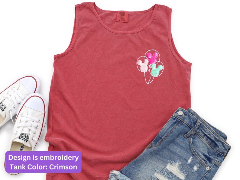 May include: Crimson tank top with embroidered Mickey Mouse balloon design. The sleeveless shirt is paired with denim shorts and white sneakers. The design features three balloons in pink, green, and pink.