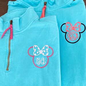 May include: Two turquoise blue quarter-zip sweatshirts with embroidered Minnie Mouse ears and bows. One sweatshirt has the monogram "BHL" and the other has the monogram "JSM".