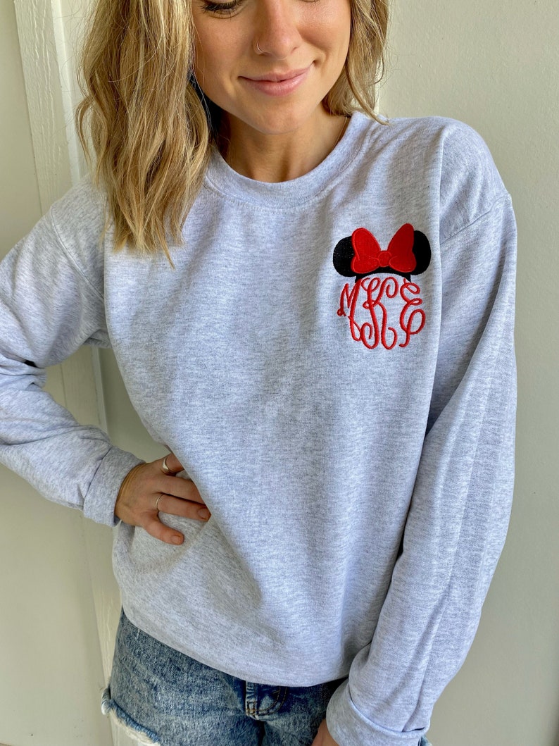 Puede incluir: Sudadera gris con un dise&ntilde;o de orejas de Minnie Mouse bordado en rojo y un monograma. El monograma es rojo e incluye las letras M, S y L.