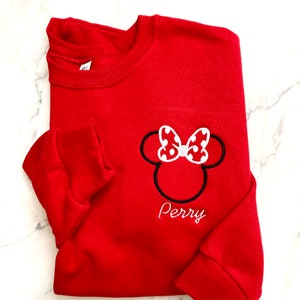 May include: Red sweatshirt with a white and black embroidered Minnie Mouse head with a red bow and white polka dots. The name "Perry" is embroidered below the image.