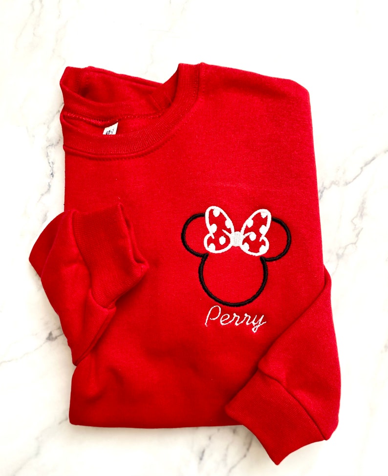 May include: Red sweatshirt with a white and black embroidered Minnie Mouse head with a red bow and white polka dots. The name "Perry" is embroidered below the image.