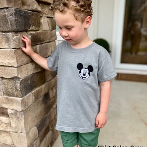 May include: A grey t-shirt featuring a black and white Mickey Mouse graphic on the chest. The shirt is paired with green shorts. The text "Shirt Color: Grey" is visible at the bottom of the image.