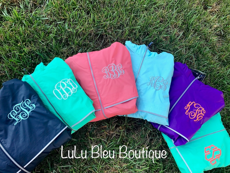 May include: Six different color lightweight jackets with reflective trim and personalized monograms. The jackets are laid out on a bed of green grass. The text "Lulu Bleu Boutique" is visible in the center of the image.