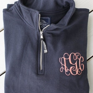 Może przedstawiać: Granatowa bluza rozpinana na 1/4 z haftowanym monogramem "CGG" w jasnor&oacute;żowym kolorze. Bluza ma zamek błyskawiczny z metką "Castles River".