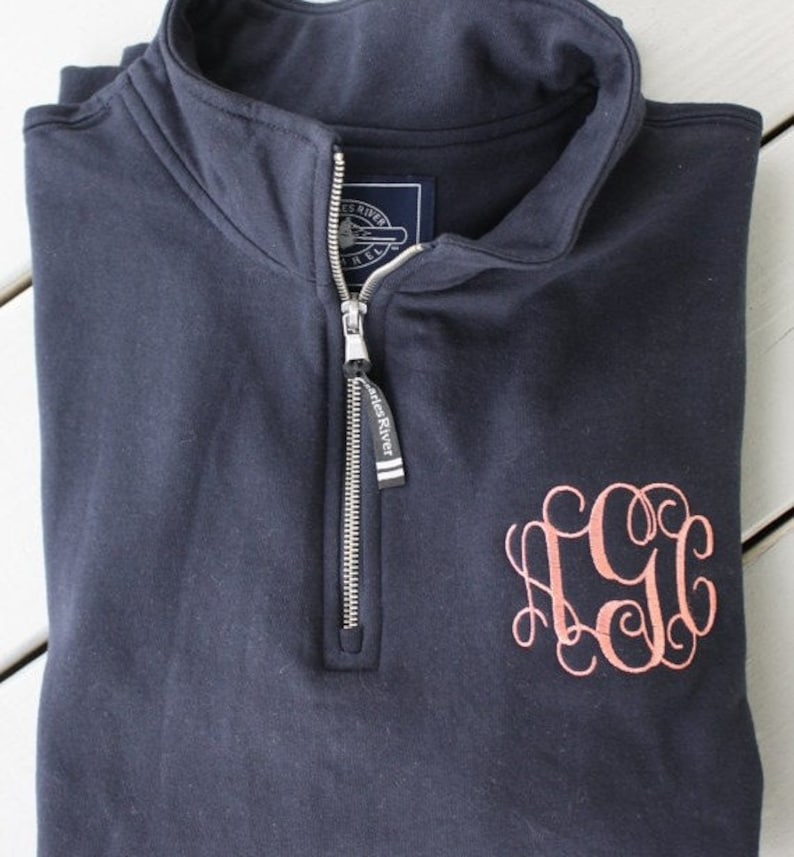Może przedstawiać: Granatowa bluza rozpinana na 1/4 z haftowanym monogramem "CGG" w jasnor&oacute;żowym kolorze. Bluza ma zamek błyskawiczny z metką "Castles River".