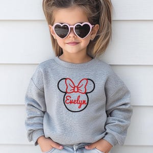 May include: A grey sweatshirt with a black and red embroidered Minnie Mouse head with a bow and the name "Evelyn" underneath.