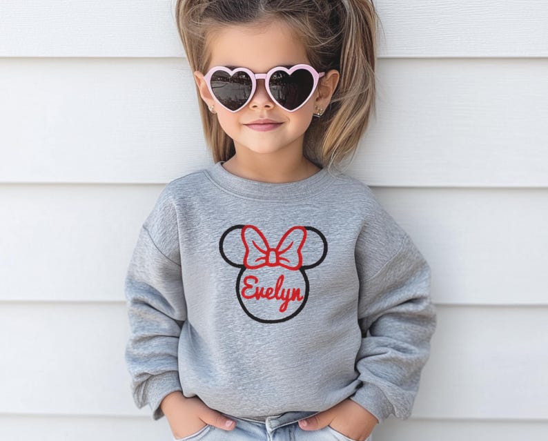 May include: A grey sweatshirt with a black and red embroidered Minnie Mouse head with a bow and the name "Evelyn" underneath.