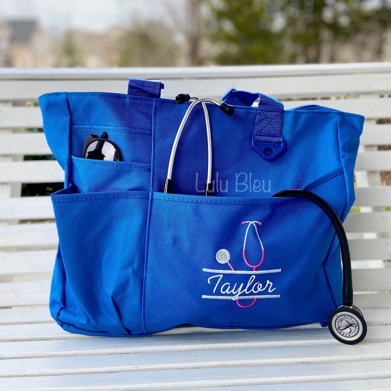 Puede incluir: Una bolsa de lona azul con un estetoscopio y el nombre "Taylor" bordado. La bolsa tiene varios bolsillos y un cierre de cremallera. La bolsa est&aacute; sobre una superficie de madera blanca.