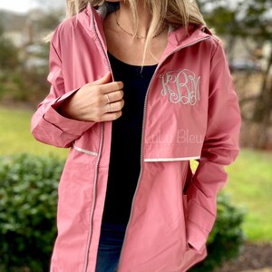 May include: A pink hooded raincoat with a white zipper and reflective trim. The raincoat has a monogrammed "KRM" on the front. The text "Lulu Bleu" is visible on the bottom right of the raincoat.
