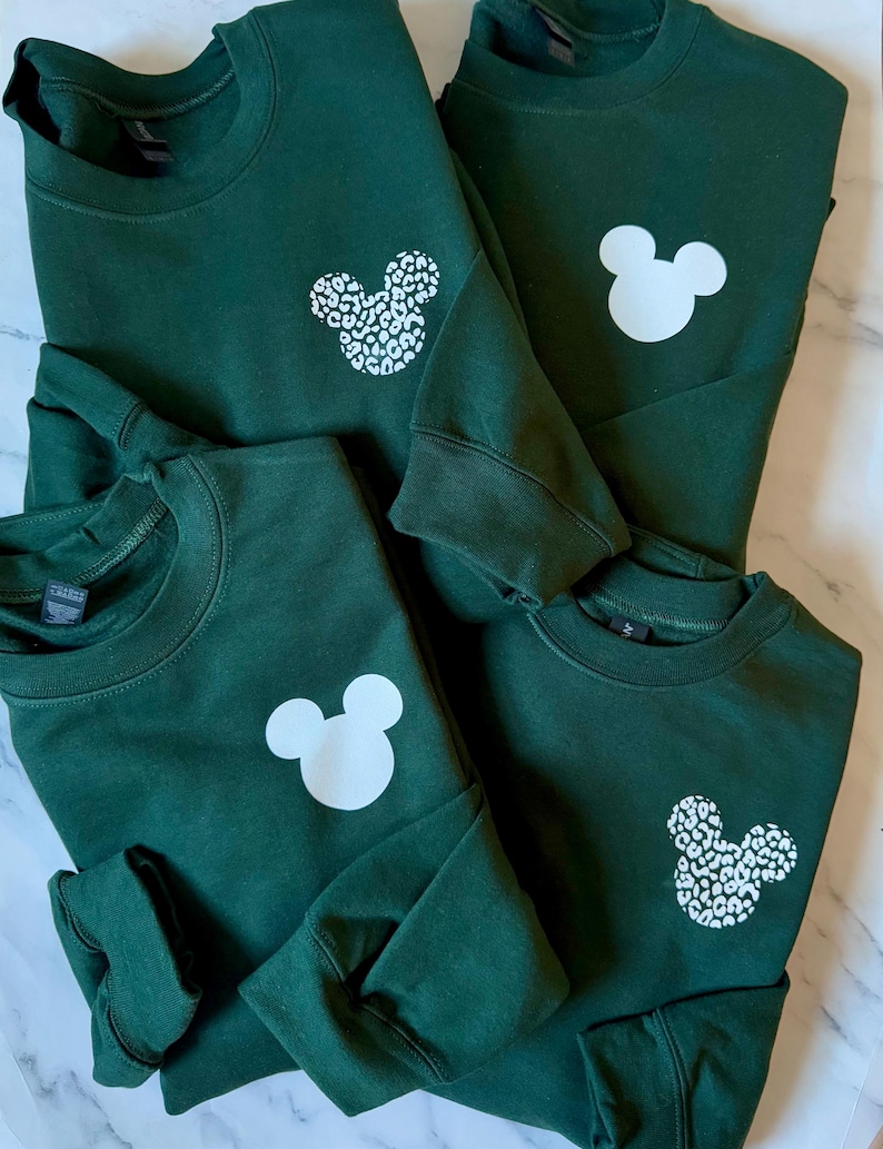 May include: Four green sweatshirts with white Mickey Mouse designs. One sweatshirt has a solid white Mickey Mouse, one has a leopard print Mickey Mouse, and two have a solid white Mickey Mouse.