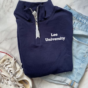 May include: A navy blue quarter-zip sweatshirt with white embroidered text that reads "Lee University".