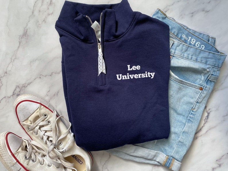 May include: A navy blue quarter-zip sweatshirt with white embroidered text that reads "Lee University".
