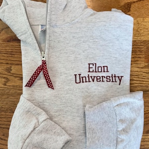 May include: A gray sweatshirt with a red zipper and a red embroidered logo that says "Elon University".