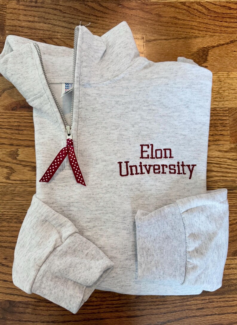 May include: A gray sweatshirt with a red zipper and a red embroidered logo that says "Elon University".