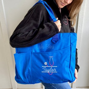 Puede incluir: Una bolsa de lona azul con un estetoscopio y el nombre "Taylor" bordado. La bolsa tiene un bolsillo con cremallera y un asa. La bolsa est&aacute; hecha por Lulu Bleu.