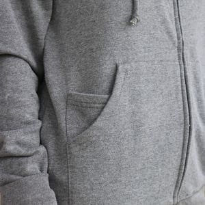 Puede incluir: Una sudadera con capucha gris con cremallera y un bolsillo canguro. La sudadera tiene una capucha con cord&oacute;n y mangas largas.