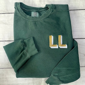 May include: A dark green sweatshirt with long sleeves and a white and gold embroidered "LL" on the front.
