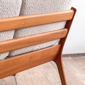 Puede incluir: Primer plano de un sof&aacute; moderno de mediados de siglo. El sof&aacute; presenta una tela texturizada de color gris claro y un marco de madera con listones horizontales. El marco de madera tiene un acabado c&aacute;lido y natural, y las patas est&aacute;n en &aacute;ngulo.