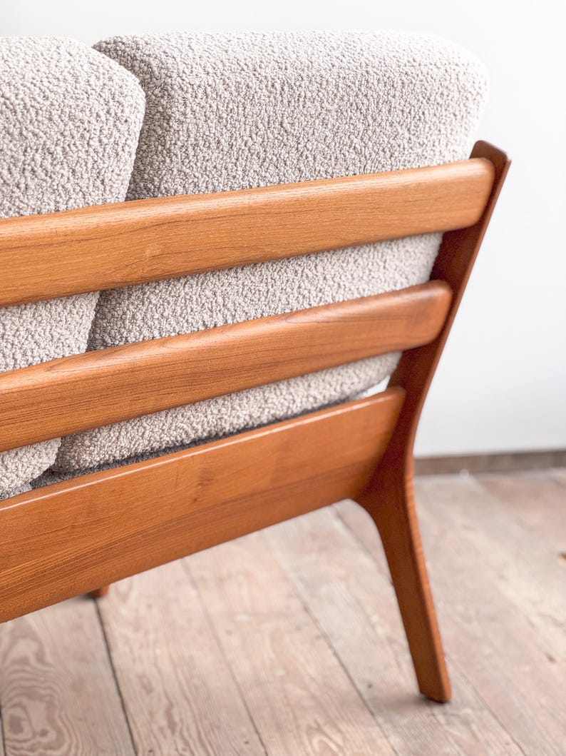 Puede incluir: Primer plano de un sof&aacute; moderno de mediados de siglo. El sof&aacute; presenta una tela texturizada de color gris claro y un marco de madera con listones horizontales. El marco de madera tiene un acabado c&aacute;lido y natural, y las patas est&aacute;n en &aacute;ngulo.