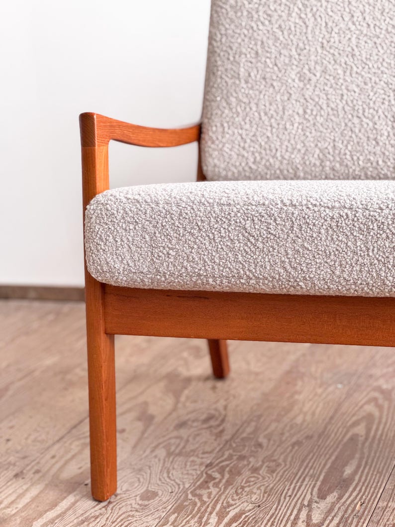 Puede incluir: Sill&oacute;n moderno de mediados de siglo con asiento y respaldo de tela texturizada gris claro. La silla tiene una estructura de madera maciza con un acabado marr&oacute;n rojizo c&aacute;lido. Los reposabrazos se curvan suavemente y las patas son rectas.