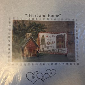 May include: A cross-stitch pattern titled "Heart and Home" featuring a red cabin, a stitched house, and the words "Health, Heart, Happiness, and Hope." The image includes a sprig of evergreen and the maker's name, "Stitches By Cheri."